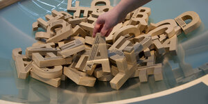 Eine Hand greift in eine Schüssel mit Holzbuchstaben.